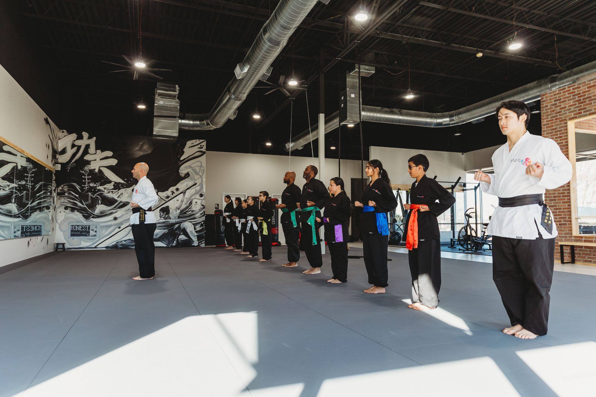 After: an adult class lined up on the finished training floor in front of the mural at Kung Fu Academy of North Texas in McKinney, TX